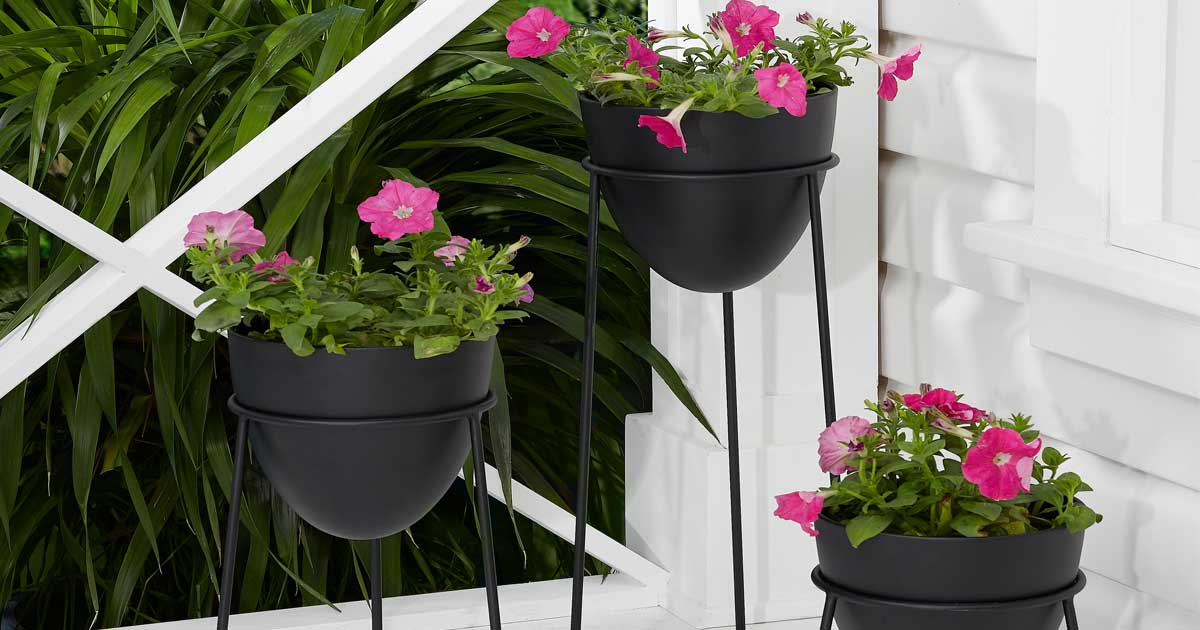 set of three black planters on a porch with flowers in them