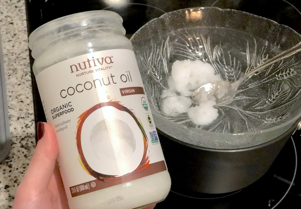 hand holding an open jar of coconut oil next to bowl of melting oil