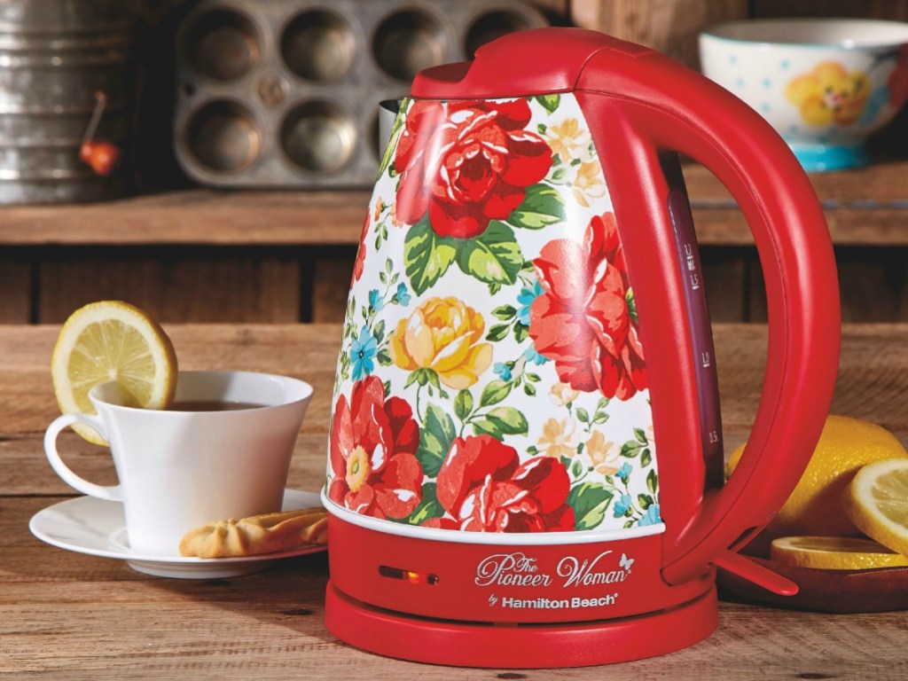 kettle in vibrant red color on counter by tea cup and lemons