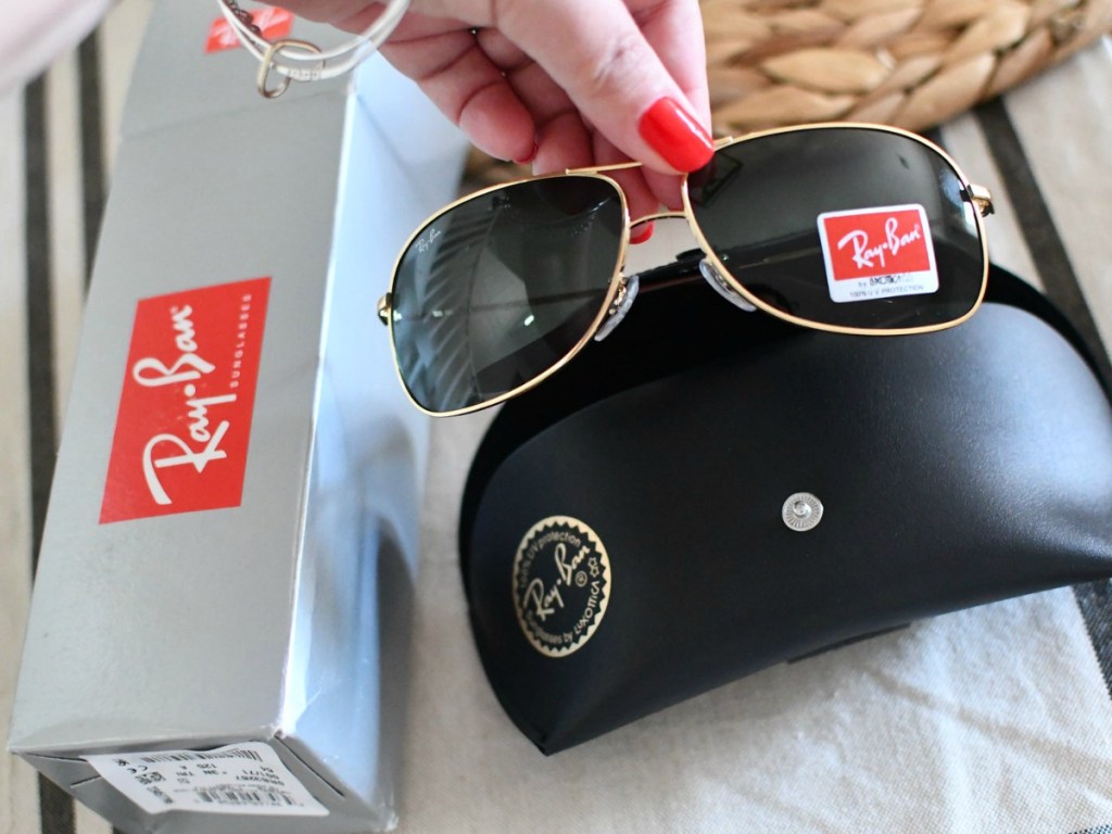 hand holding sunglasses by case and box on table