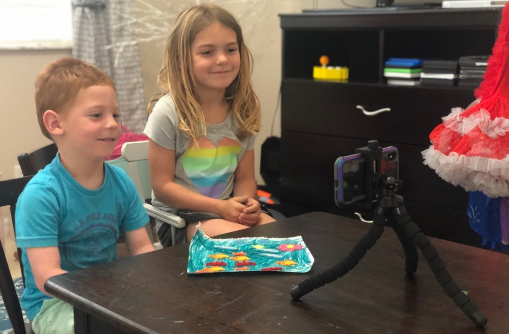 two kids sitting in front of phone on tripod smiling