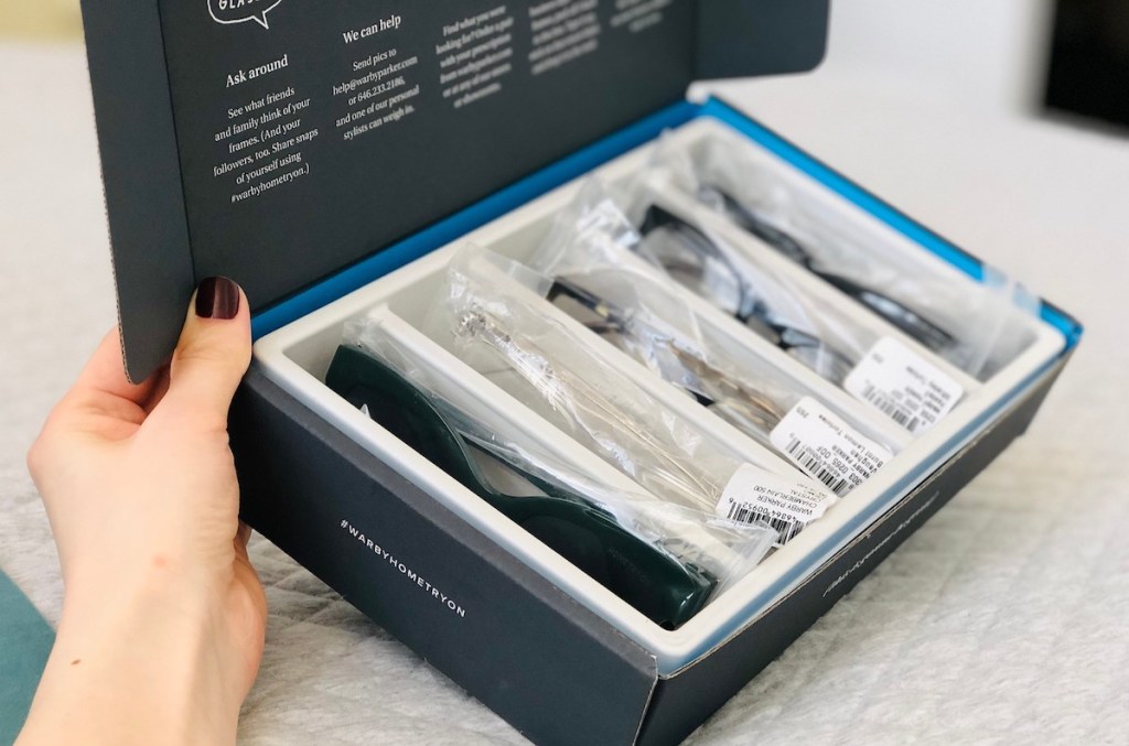 hand holding a box full of sample eyeglasses and sunglasses