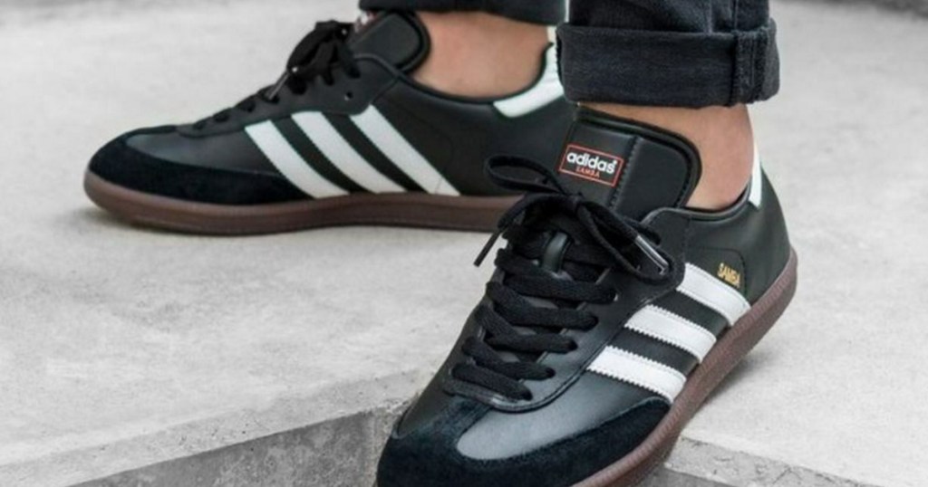 man wearing black Adidas soccer shoes on concrete outside