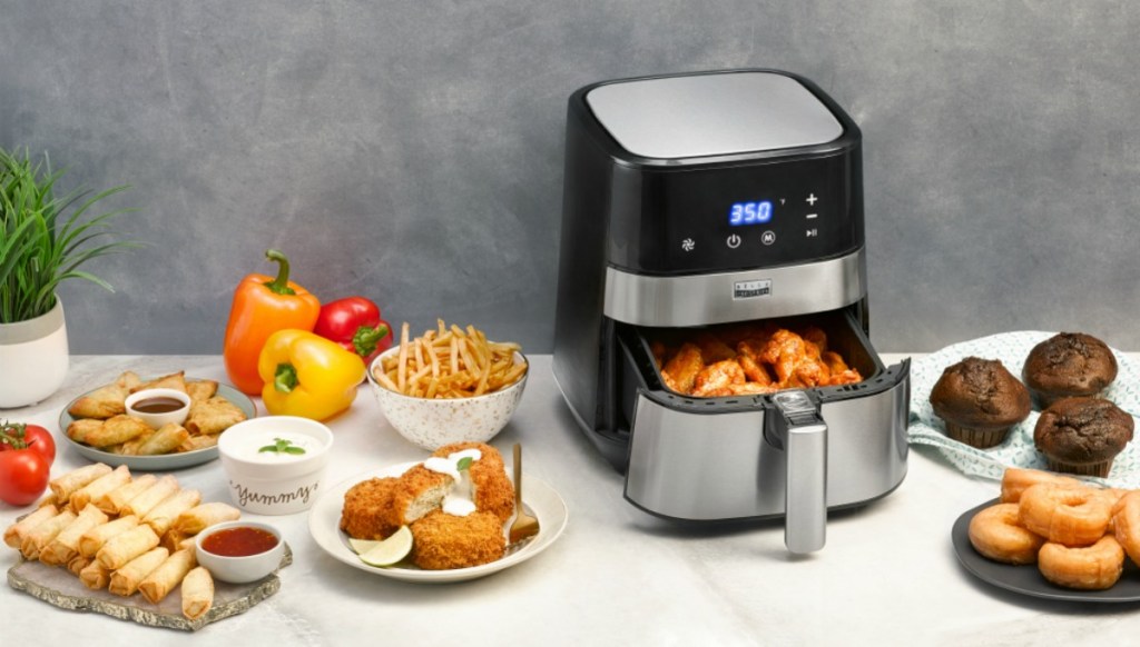 black and silver air fryer on counter surrounded by fried foods