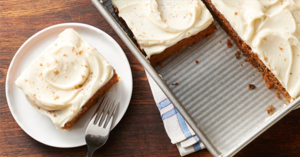 slice of carrot cake with icing on top on plate with fork with a full cake in the pan