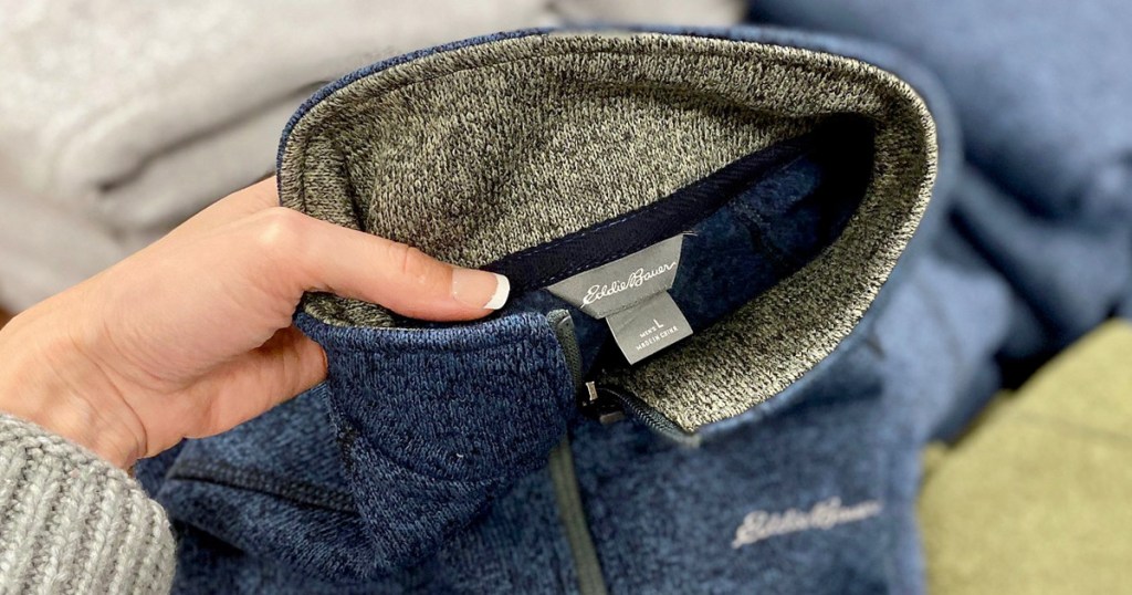 womans hand holding up a blue and grey eddie bauer brand sweater