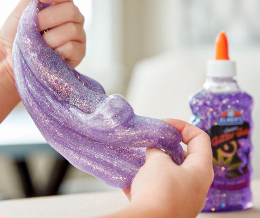 child playing with purple glitter slime with bottle of elmer's purple glitter glue in background