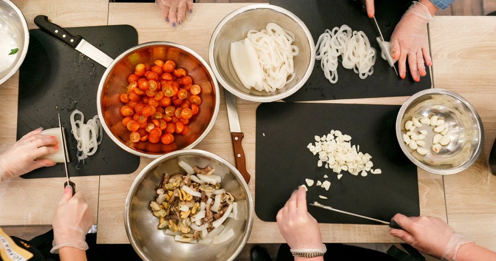 people wearing gloves chopping up ingredients like onions, garlic, and tomatoes and placing them in metal bowls