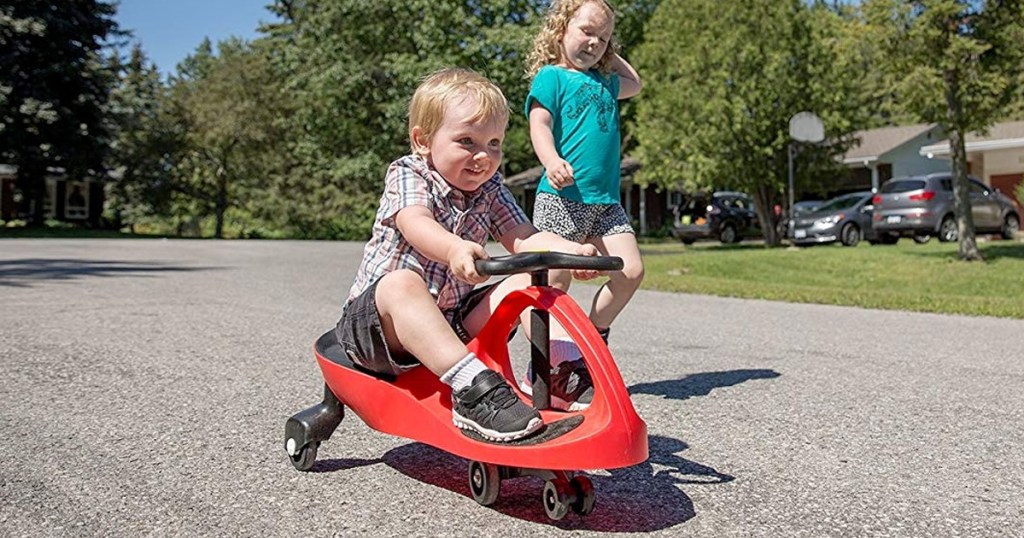 little boy playing on red and black swing car in neighborhood