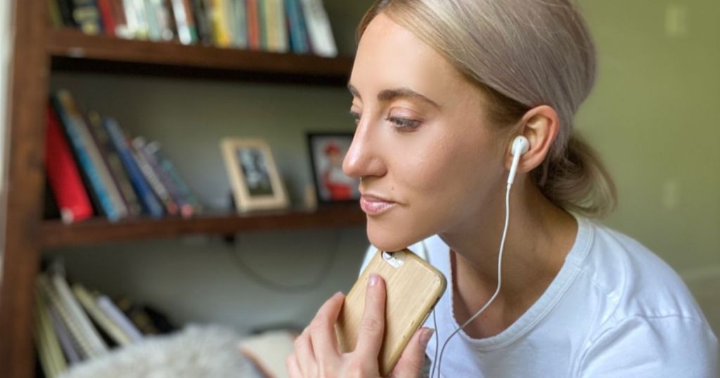 Woman holding iphone and listening to a podcast with headphones in 