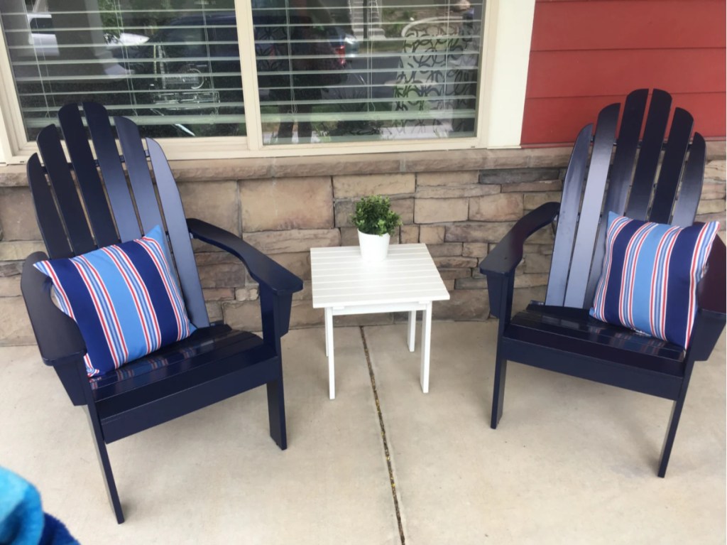 two dark blue Adirondack chairs on concrete outside home next to small white table