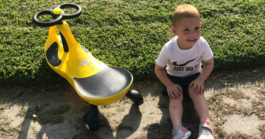 boy sitting on grass next to a yellow and black swing car