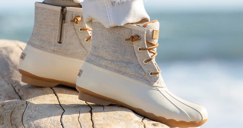 person standing on driftwood wearing white duck boots