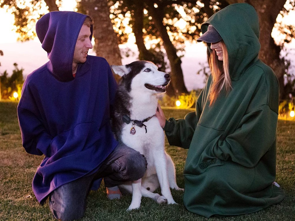 man and woman and dog sitting in blanket sweatshirts outdoors