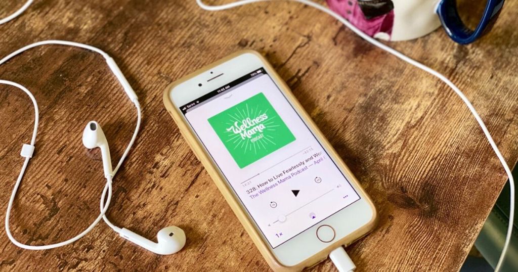 Headphones and an iphone displaying a podcast sitting on a desk