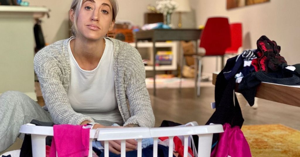 Woman sitting on the floor with a basket of laundry looking overwhelmed