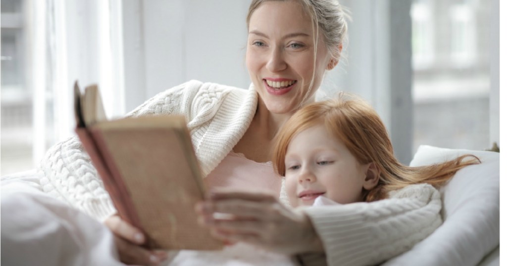 Woman reading book to child in bed