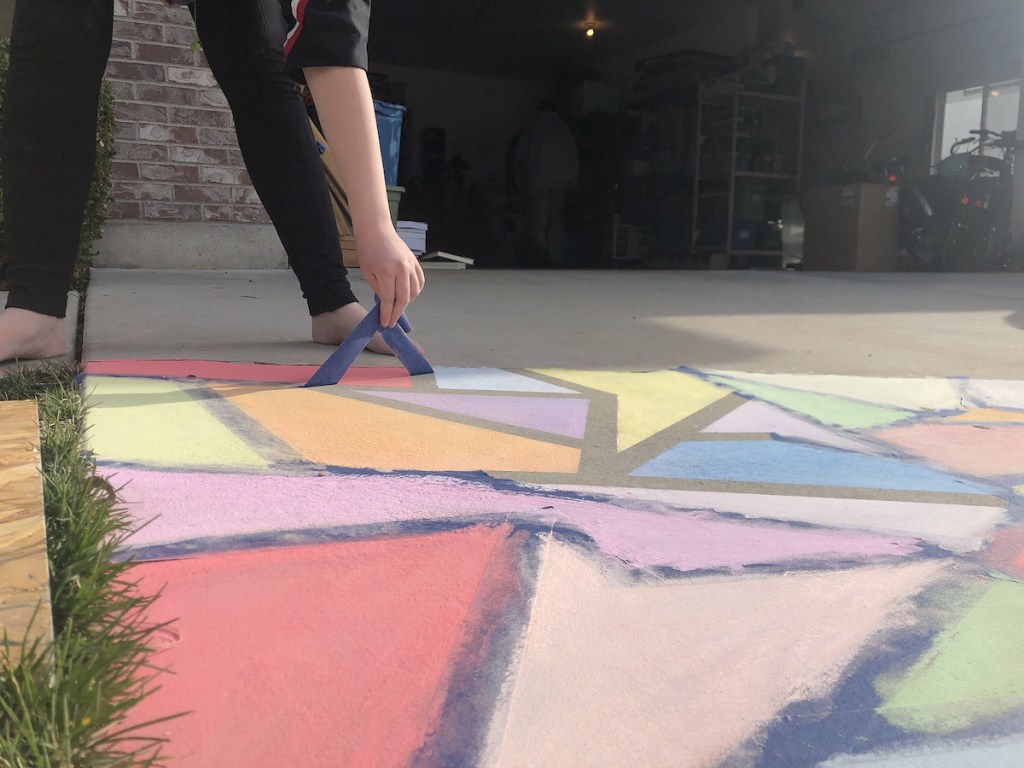 hand pulling blue painters tape of chalk colored pavement
