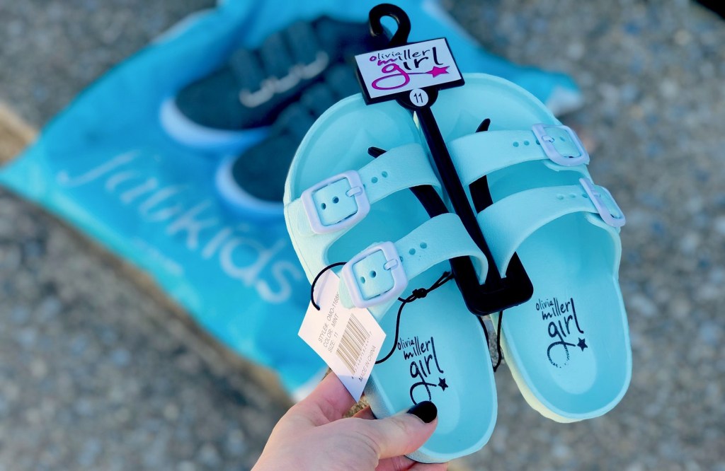 hand holding a pair of blue sandals on black hanger