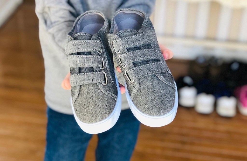 kid holding pair of gray triple velcro shoes 