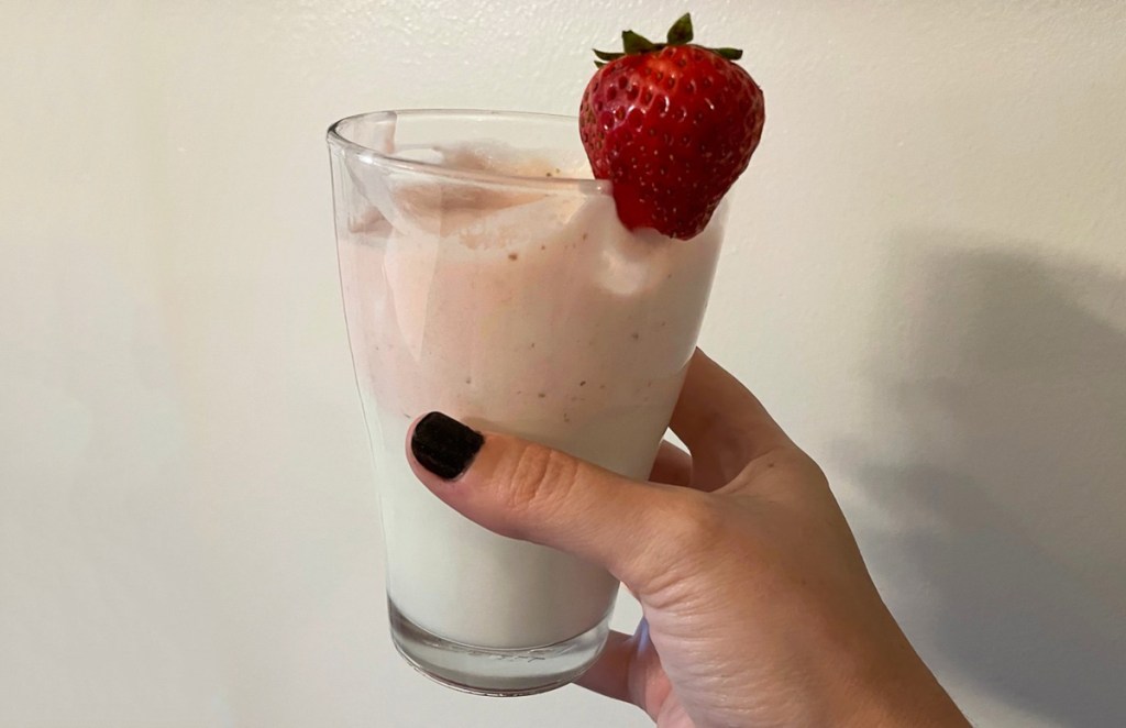 hand holding glass of strawberry whipped milk