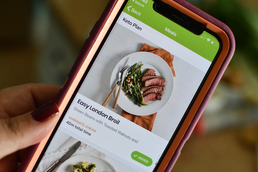 holding iPhone with eMeals Keto plan on screen