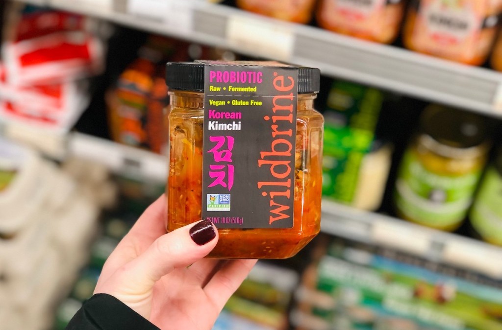 hand holding a glass jar of kimchi in store fridge aisle