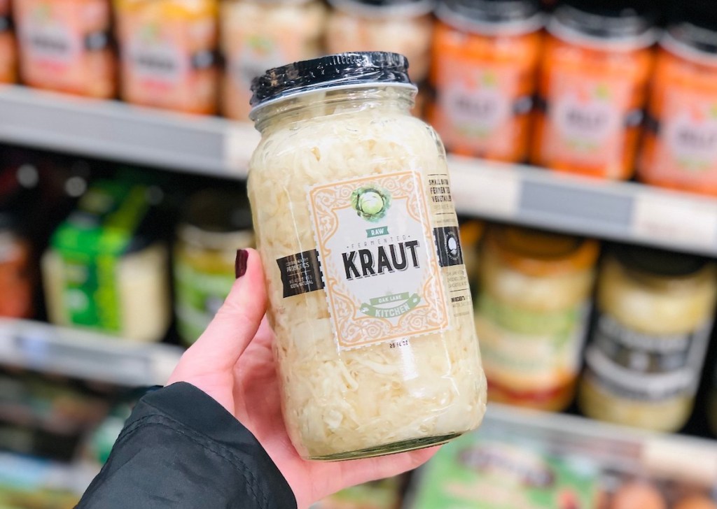 hand holding a glass jar of kraut in store fridge aisle