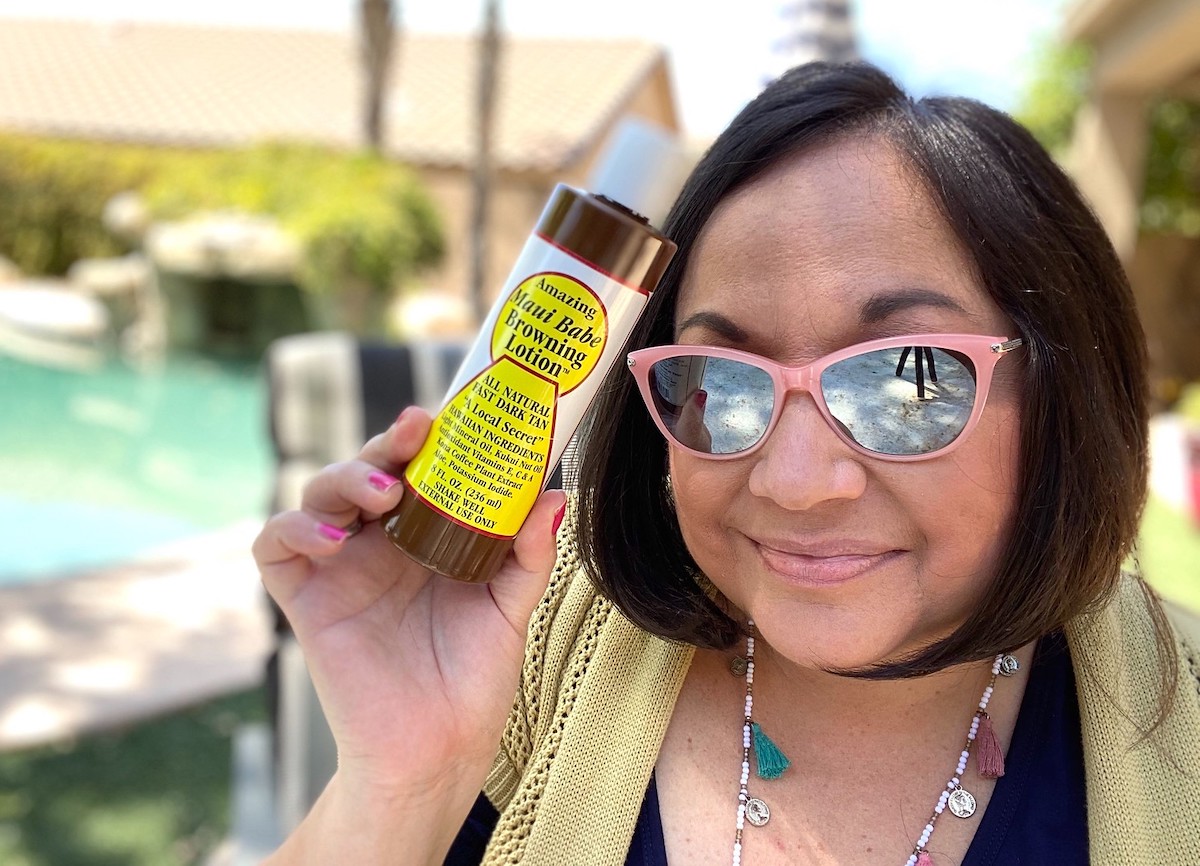 woman wearing sunglasses holding a bottle of self tanner outside