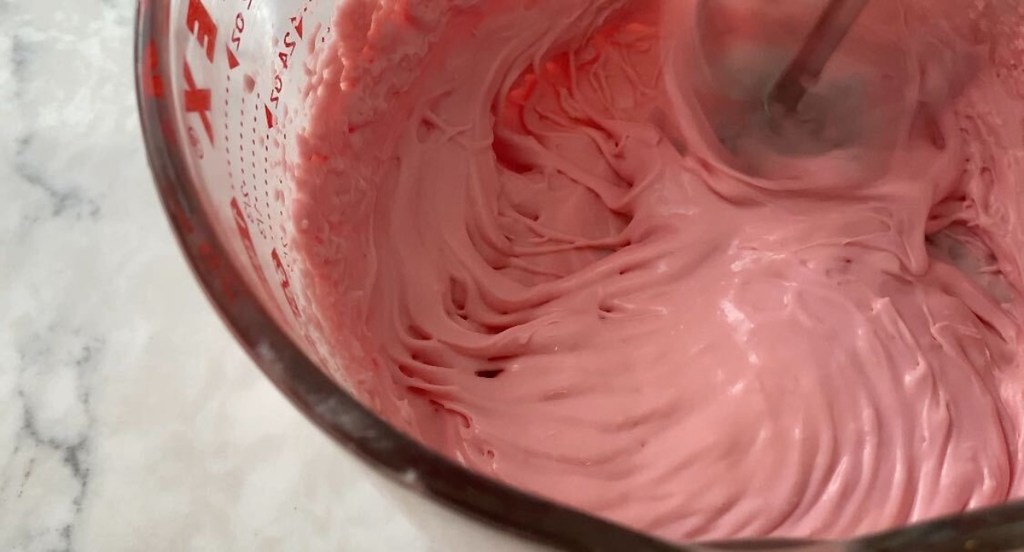 measuring bowl with mixer mixing pink fluffy liquid