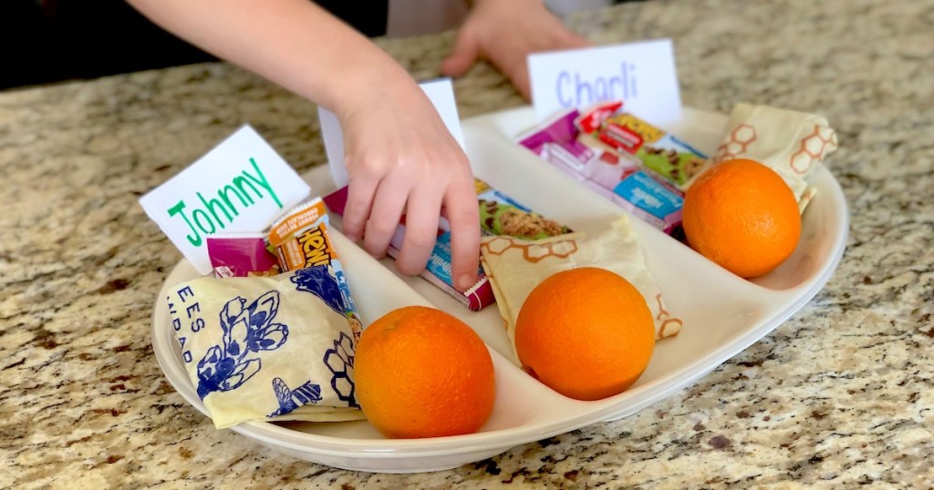 kids hand grabbing snack from snack tray with oranges bees wrapped food and snack bars