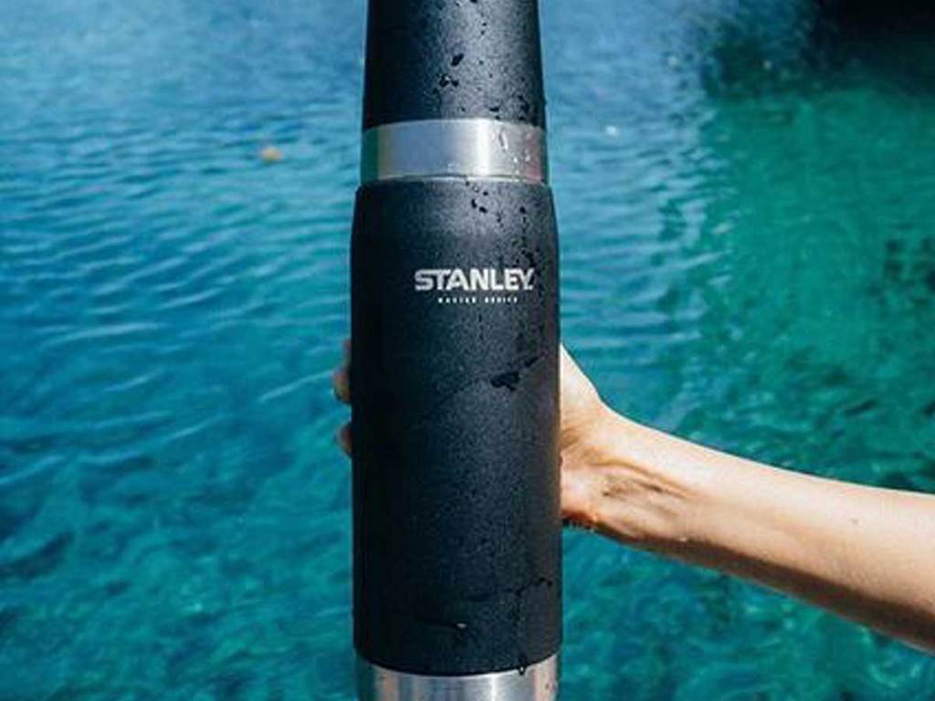 large stanley water bottle being held up over a lake