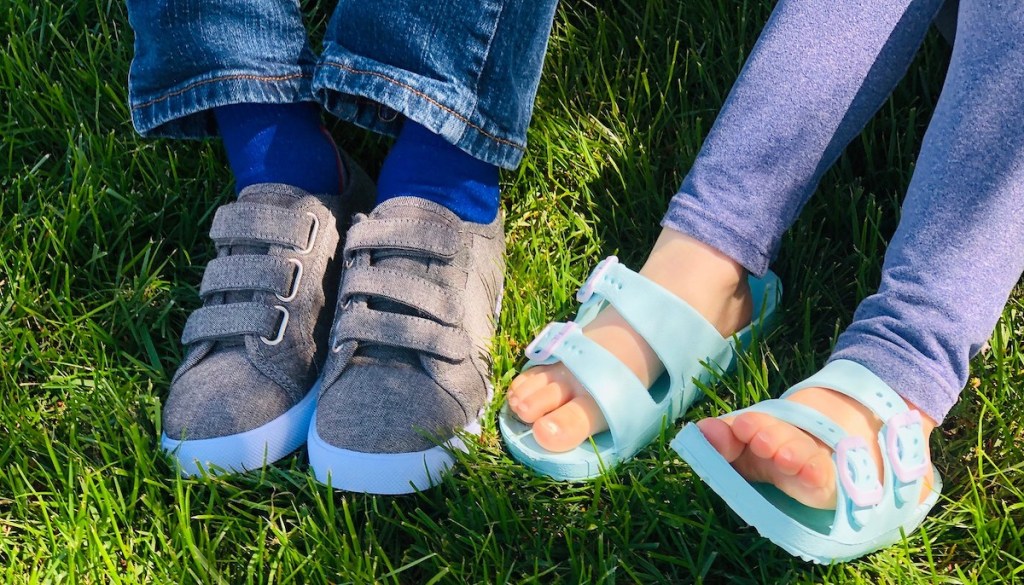 Two kids wearing a pair of gray Velcro shoes and blue sandals