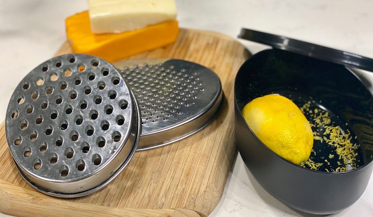 Amazon cheese grater and citrus zester with storage compartment sitting on the counter with a lemon and block cheese