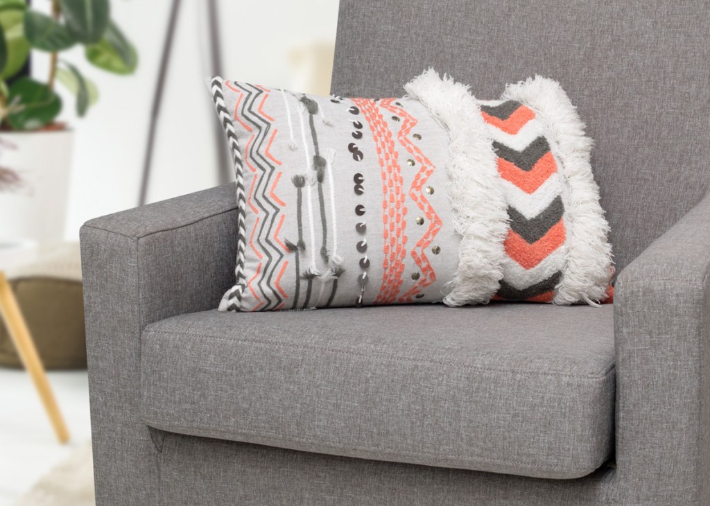 white throw pillow with grey and pink abstract chevron prints sitting on a grey chair