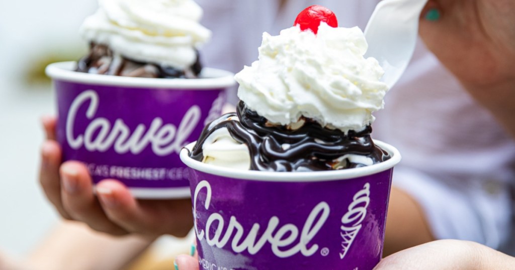 hand holding two carvel ice cream sundaes with whipped cream and cherries on top