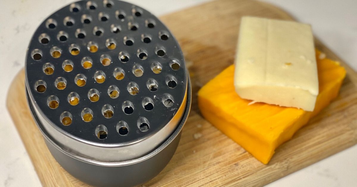 Amazon cheese grater on a cutting board next to block cheese