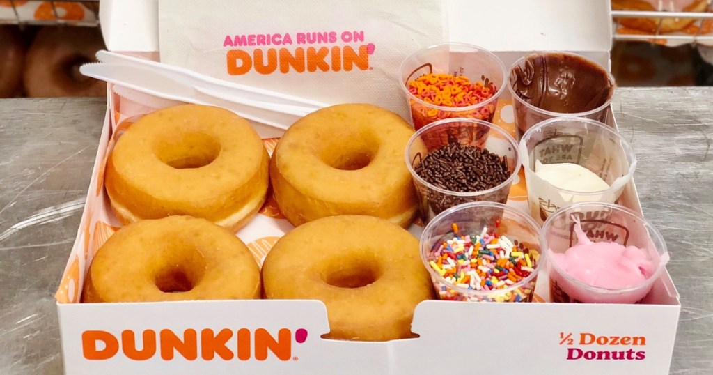 four plain donuts and cups of frosting and sprinkles inside donut box