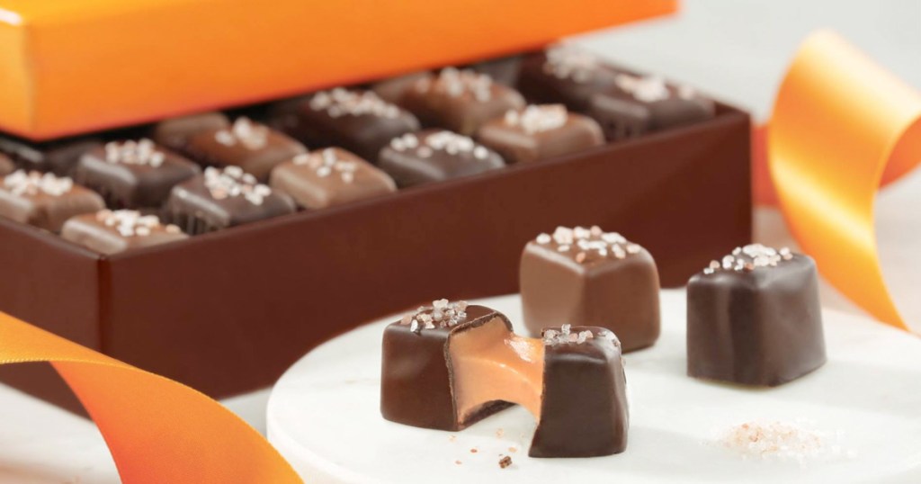 open box of chocolates with three chocolates in front, and one opened showing inside caramel