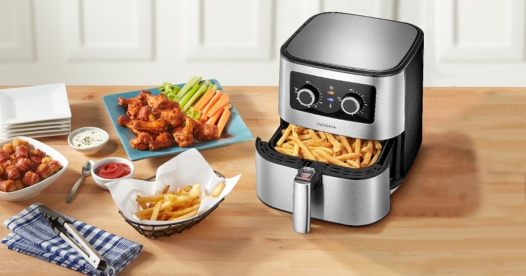 stainless steel and black air fryer on kitchen counter with basket full of fries and plates of fried foods