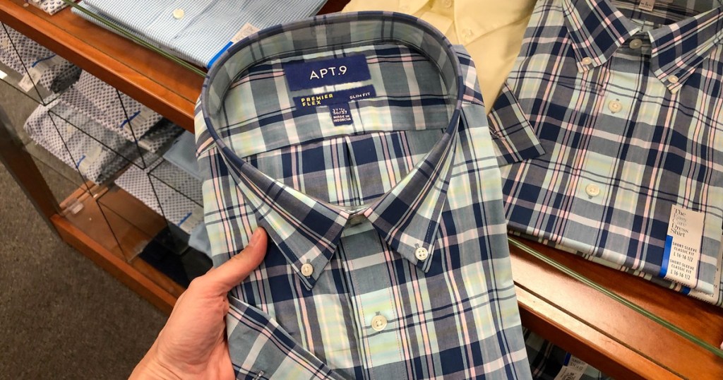 person holding up blue plaid men's dress shirt in front of store display table