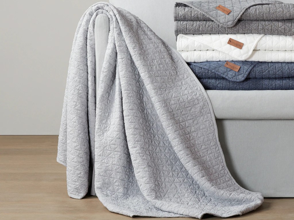 grey throw blanket next to stack of white, blue, and grey throws