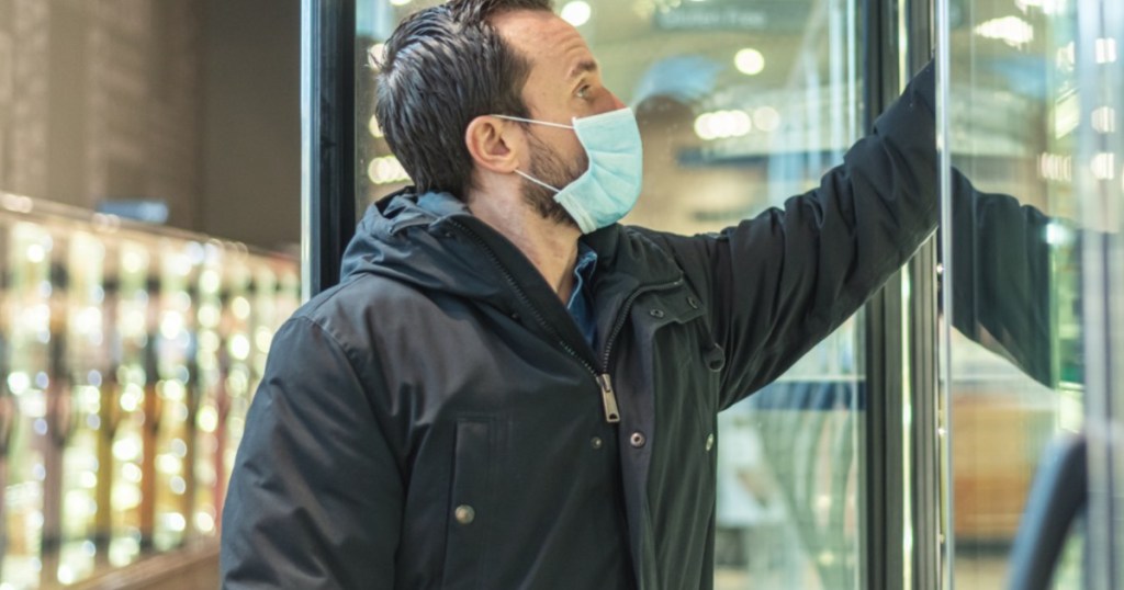 man wearing face mask reaching into freezer in store