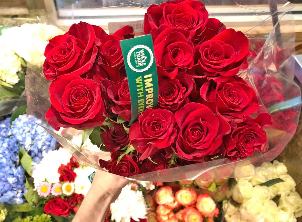 person holding a bouquet of red roses in front of flower stand