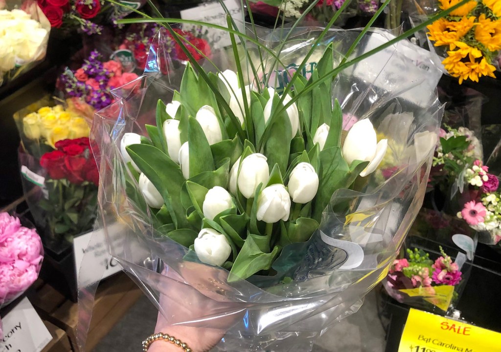 person holding a bouquet of white tulips in front of flower stand