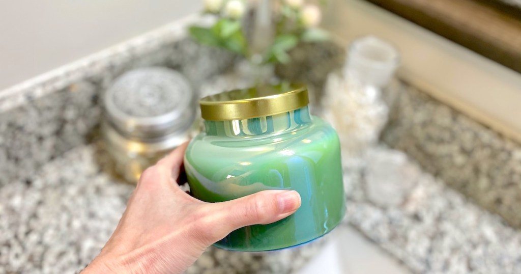 hand holding a blue green candle with gold lid