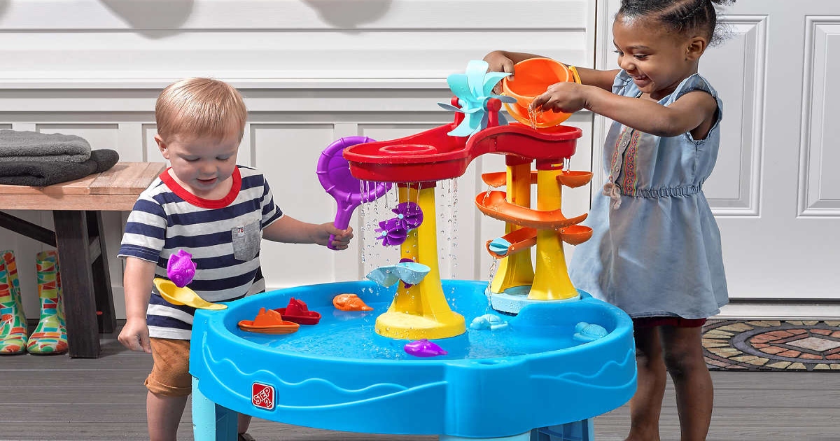 a boy and girl playing with a water table in front of a house