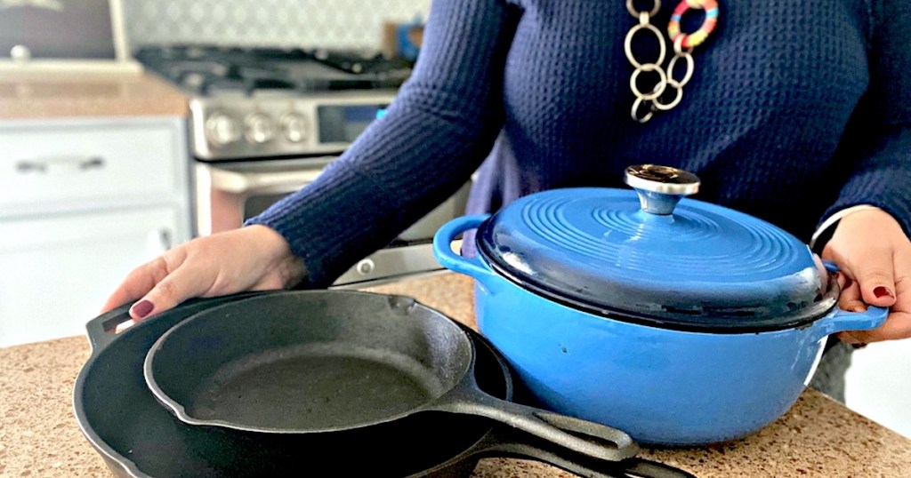 woman holding black and blue cast iron pots and pans