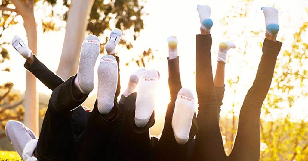 tons of people wearing white socks kicking them in the air in a park