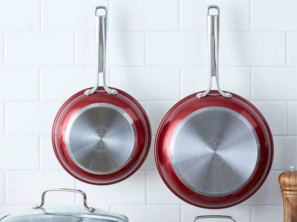 two red skillets handing on a kitchen subway tiled wall